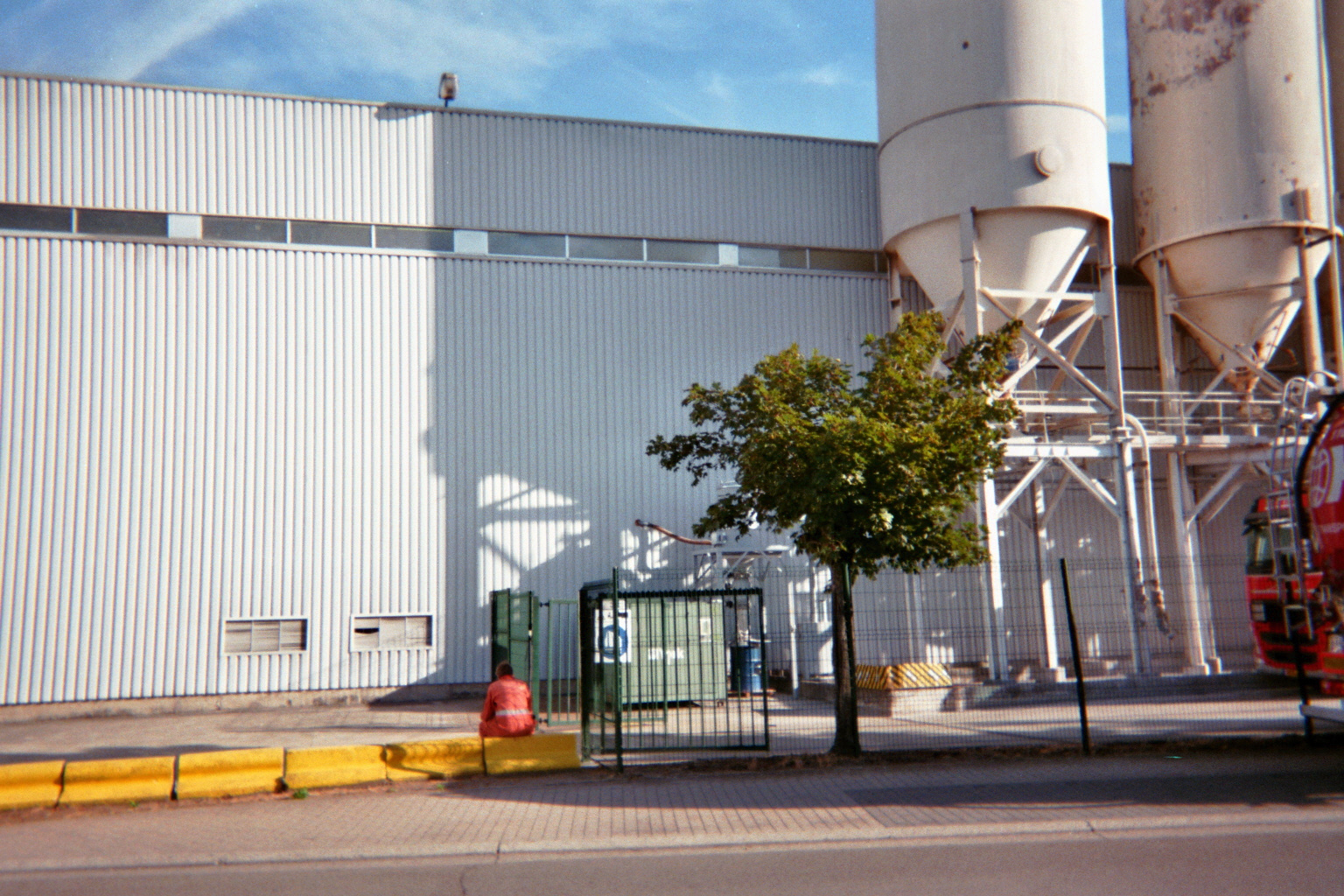 Person sitting with orange jumpsuit in front of industrial building facing away