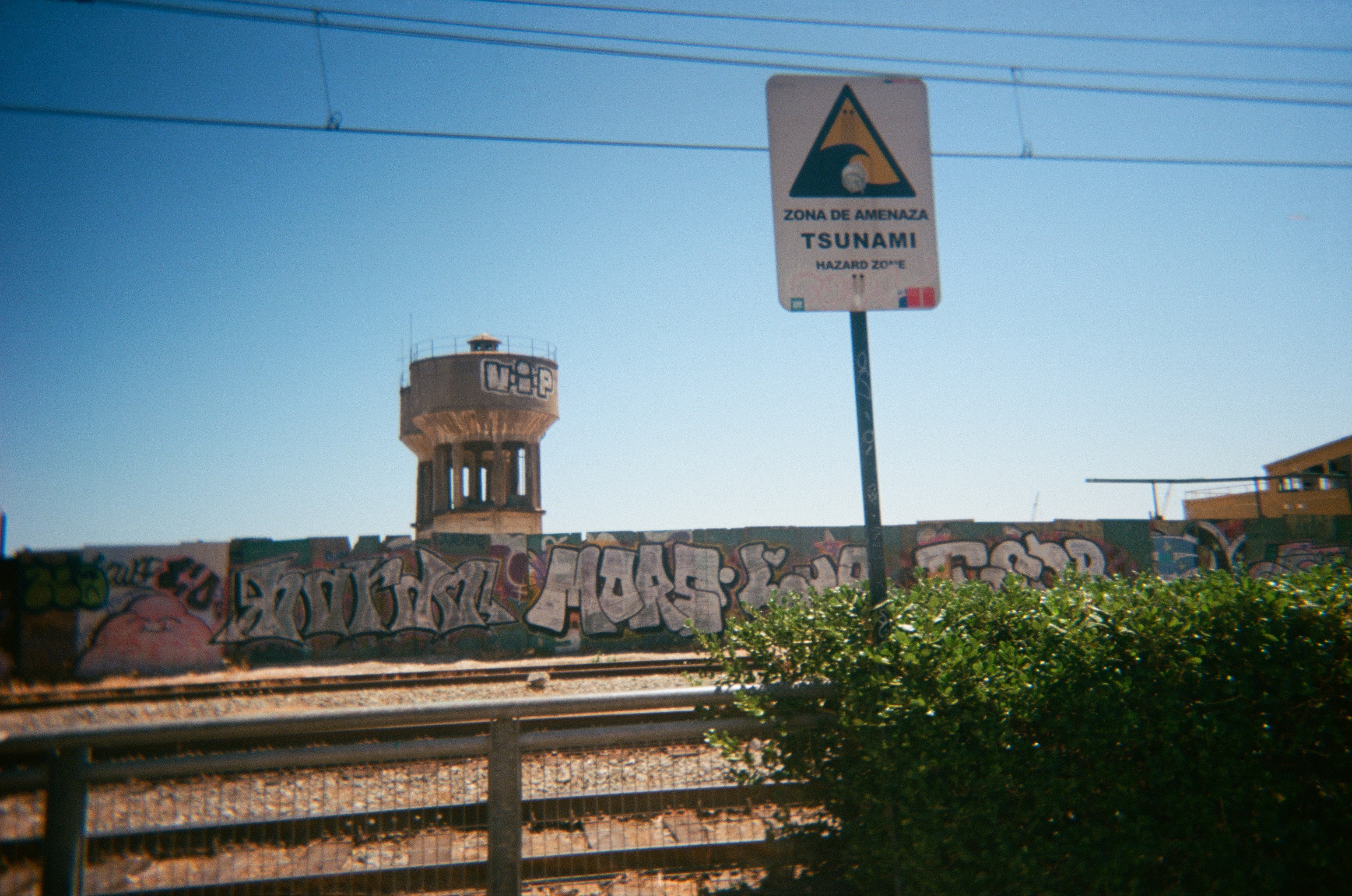 Railroads with wall full of grafiti, sign says tsunami area